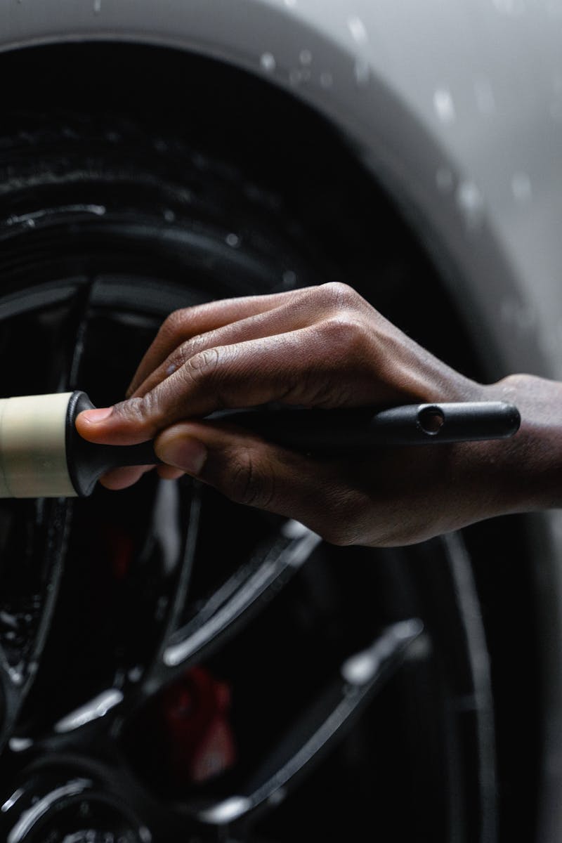 A detail-oriented close-up of a hand cleaning a car tire with a brush and soap.